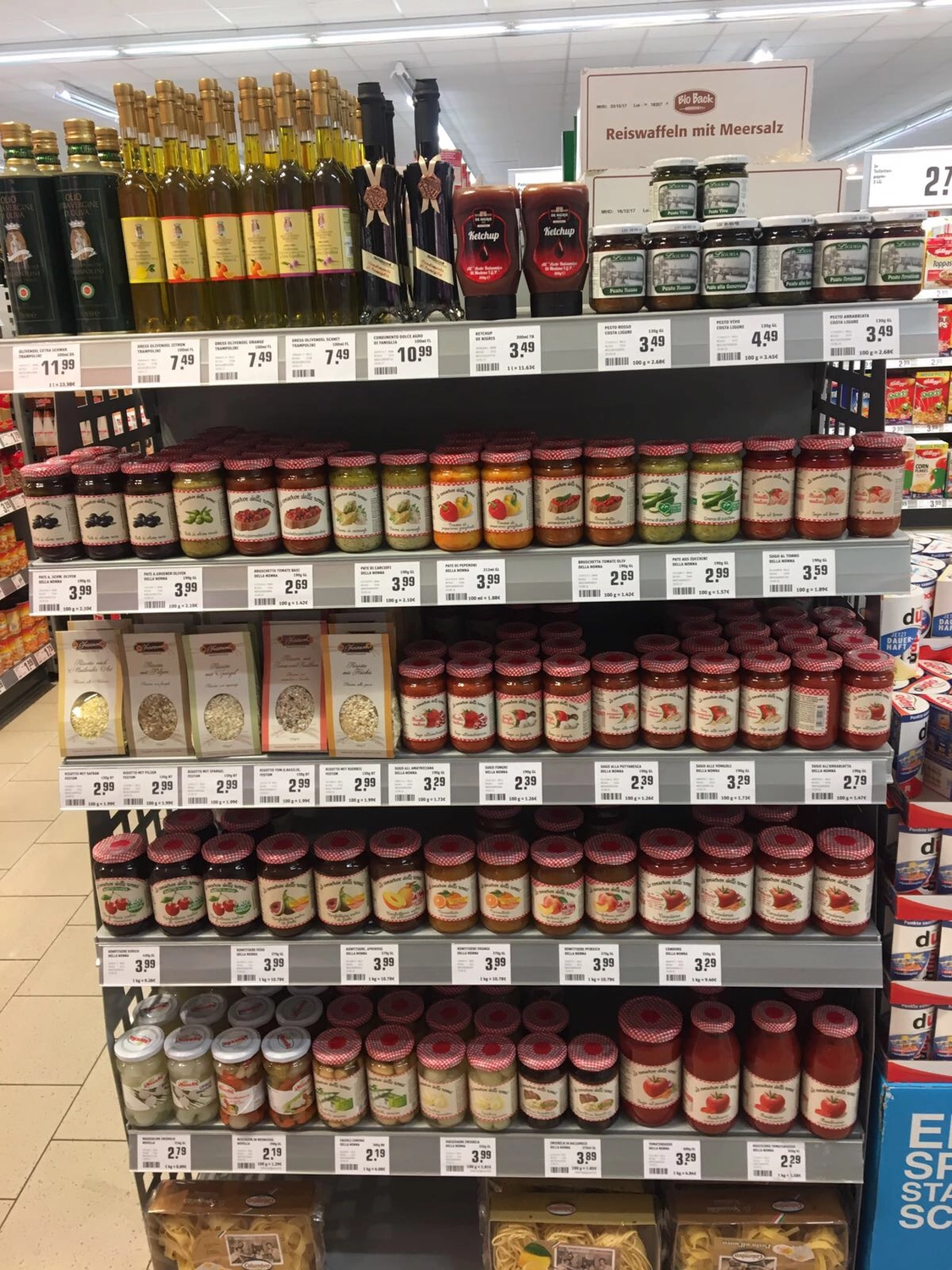 Sommerkamp Handelsvertrieb – Supermarkt – Dieses Bild zeigt ein Verkaufsregal in einem Einzelhandelsgeschäft, das mit verschiedenen Lebensmitteln in Gläsern gefüllt ist, darunter Nudelsaucen und Spezialgewürze.